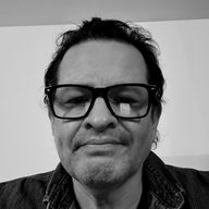 Jorge Calderon in black-framed glasses and a denim shirt